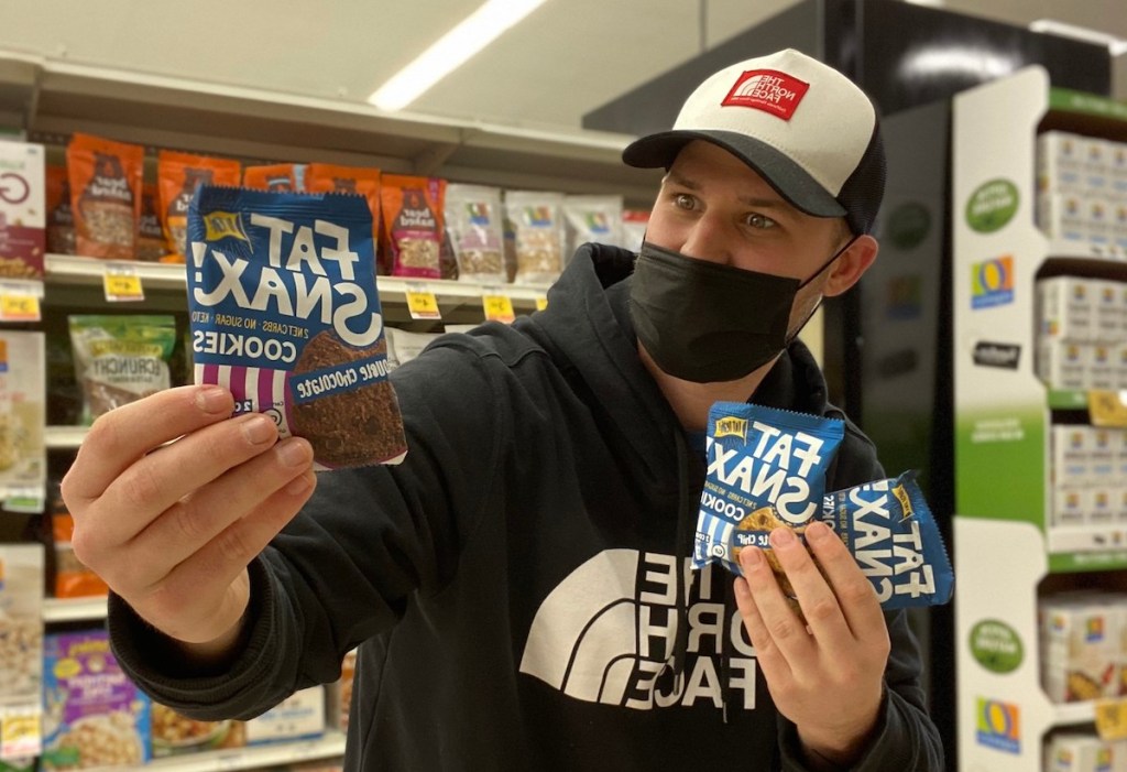 man holding fat snax cookies in store aisle