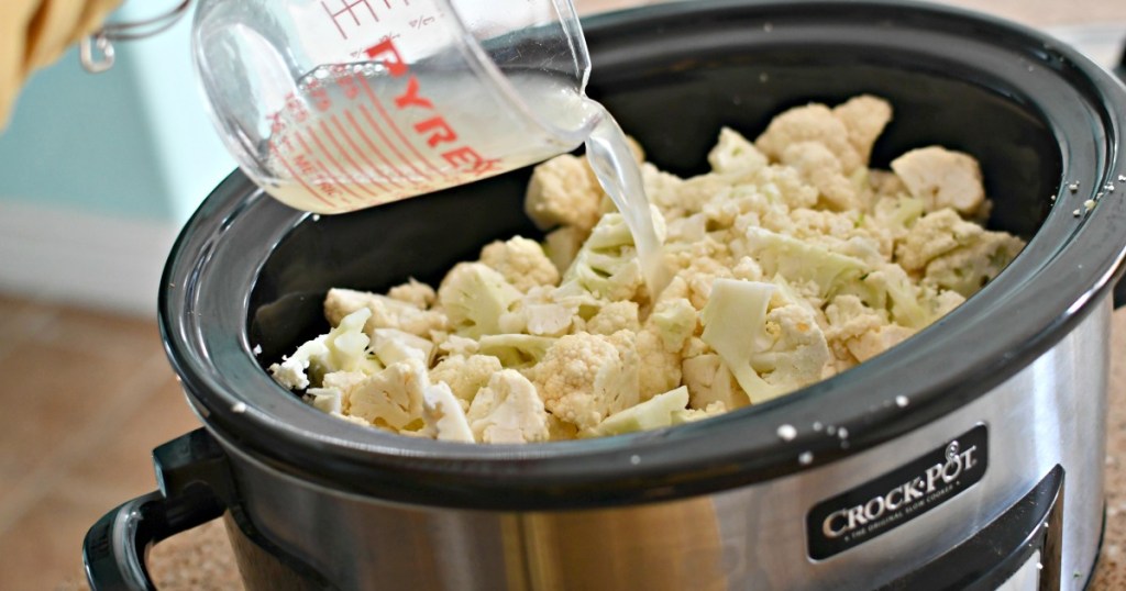 pouring broth over cauliflower in slow cooker