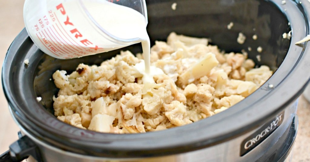 pouring cream over cooked cauliflower inside slow cooker