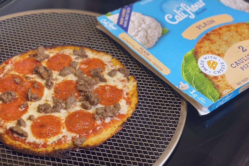 A pepperoni and sausage pizza on a pan next to a pizza crust box