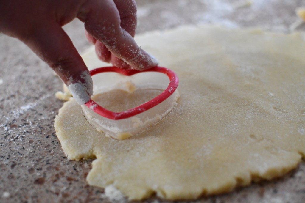 using a cookie cutter to make conversation heart cookies that are also keto sugar cookies
