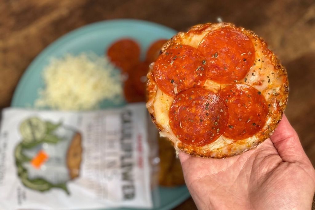 A hand holding a mini pepperoni pizza