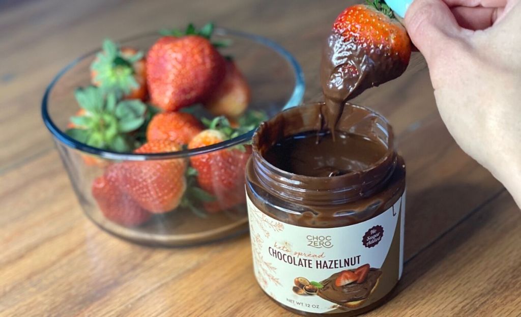 Dipping a strawberry in some chocolate spread next to a bowl of strawberries