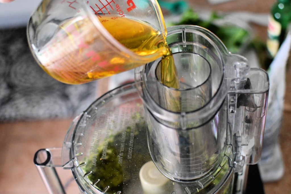 adding olive oil to pesto in food processor