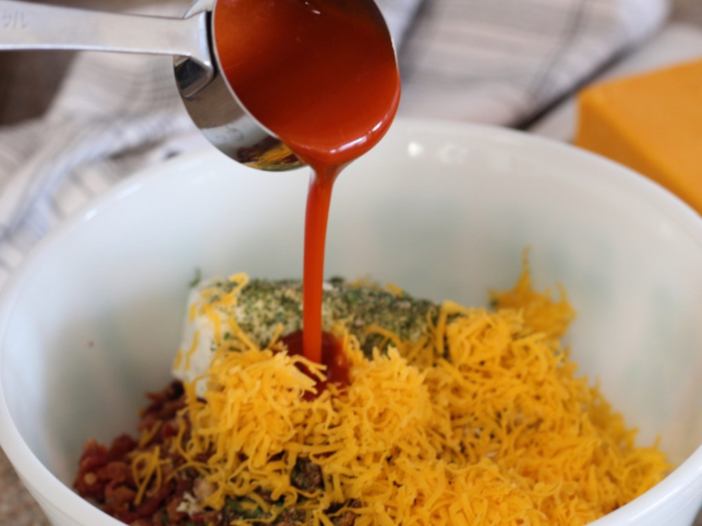 pouring buffalo sauce in mixing bowl