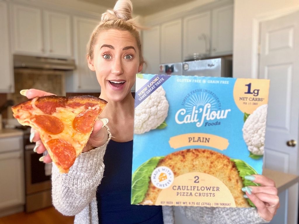 woman holding out slice of cauliflower crust pepperoni pizza 