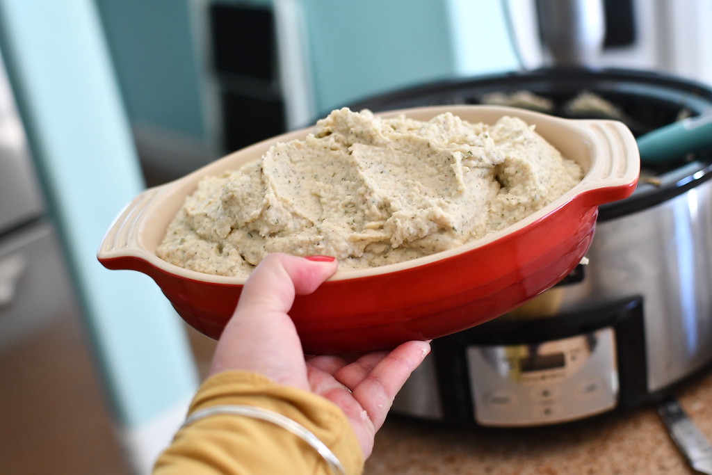 holding bowl of keto cauliflower mash by slow cooker 
