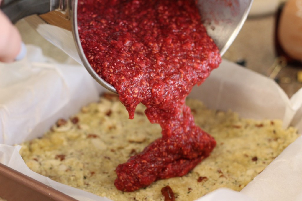 pouring raspberry filling over keto crust