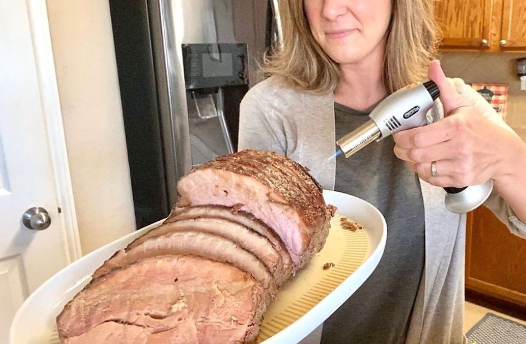 woman holding platter with cooked ham with culinary torch 