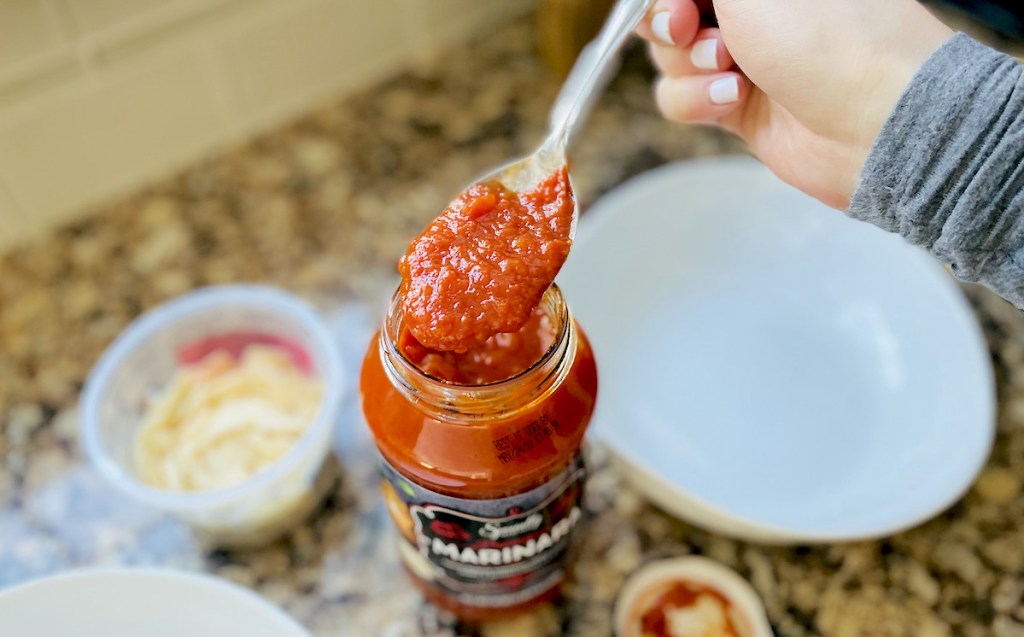 hand holding spoon from jar of red marinara sauce