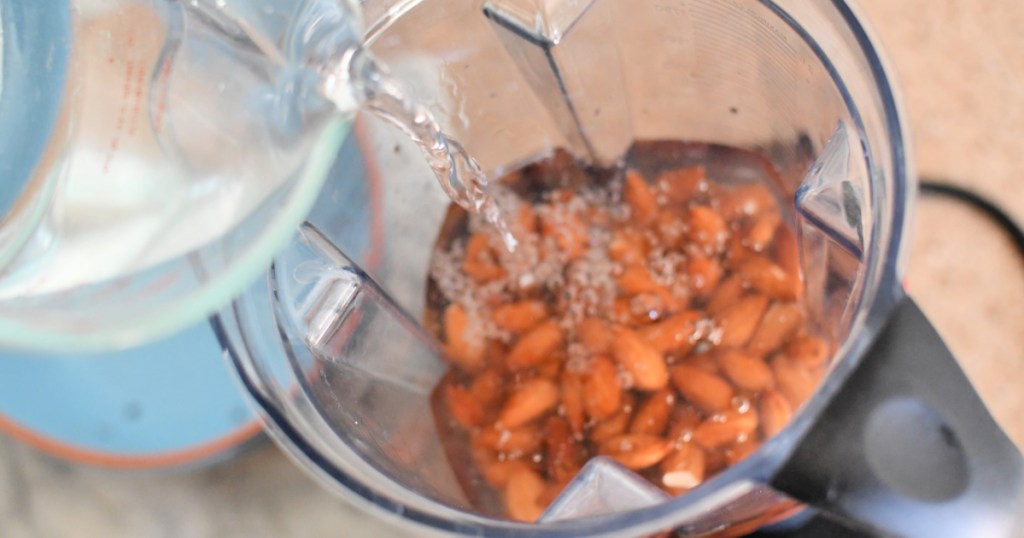 adding fresh water to soaked almonds in a blender