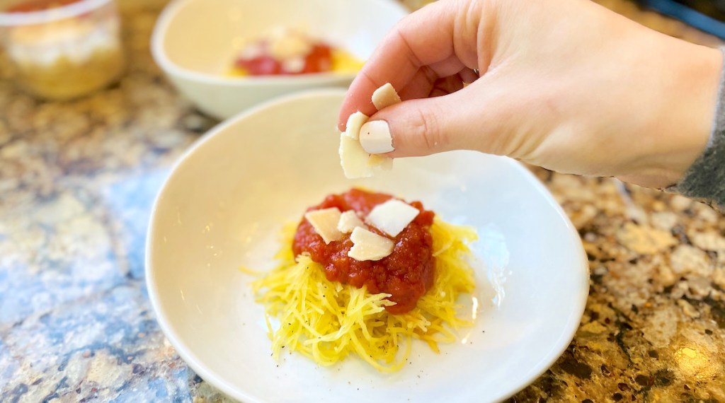 hand holding shredded cheese over bowl of yellow squash and red sauce