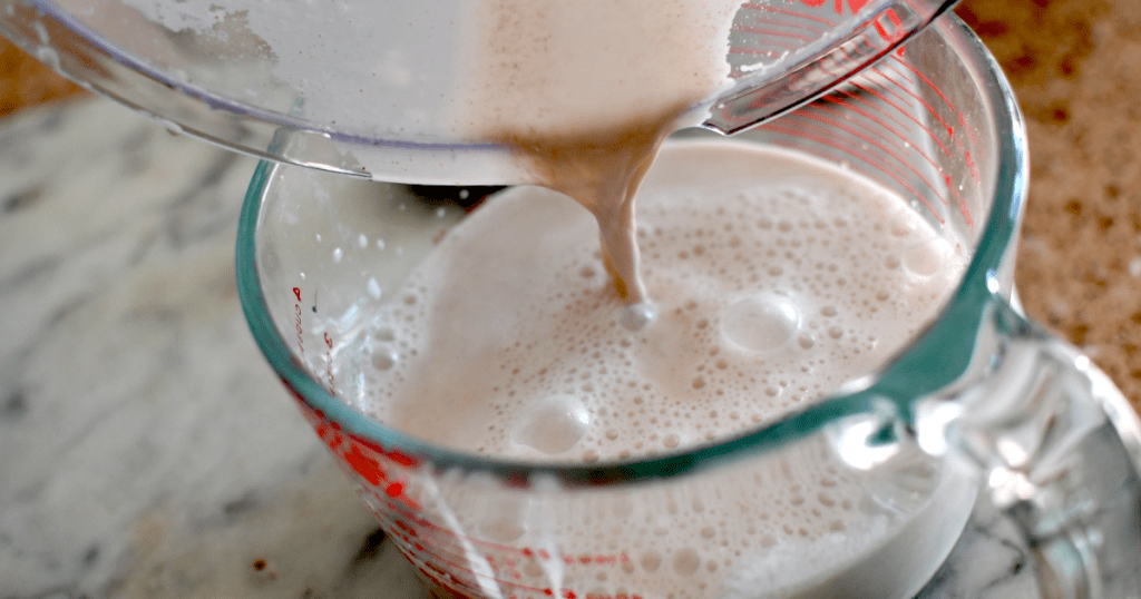 pouring homemade almond milk into measuring cup 