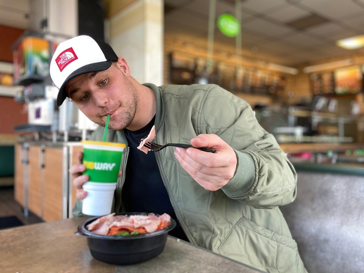 man holding Subway fountain drink and fork full of cold cuts
