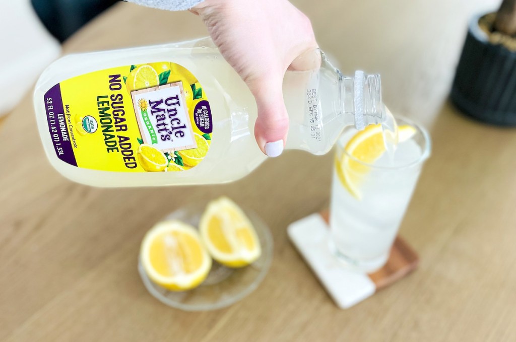 hand pouring keto sugar free lemonade into tall glass with fresh lemon