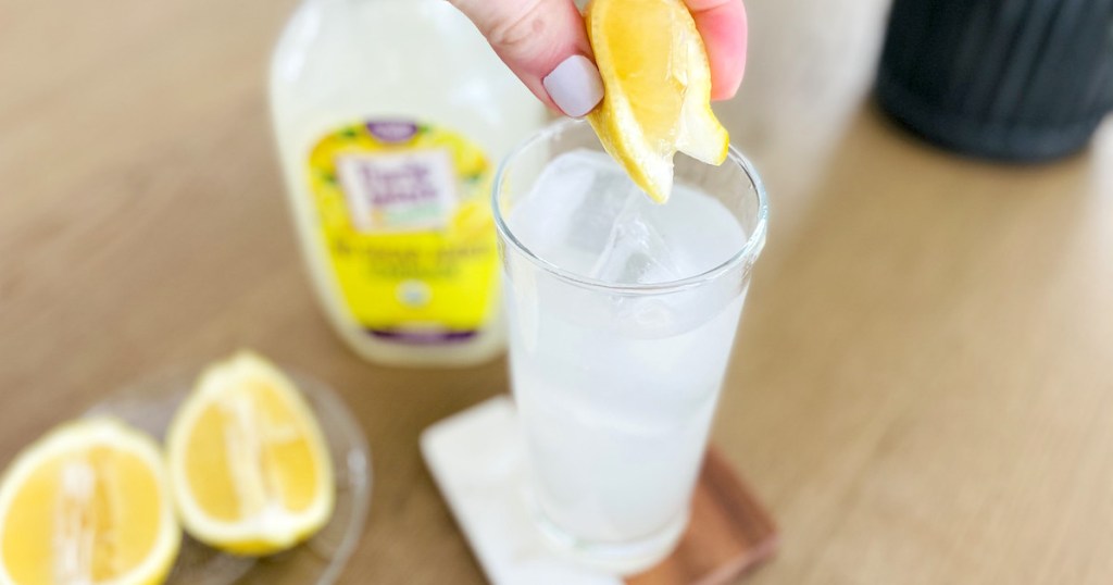 hand squeezing fresh lemon into glass of sugar free lemonade