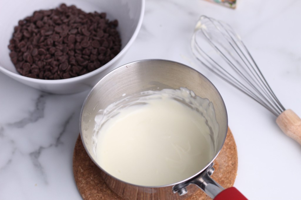 melted cream cheese in a saucepan with chocolate chips in a bowl