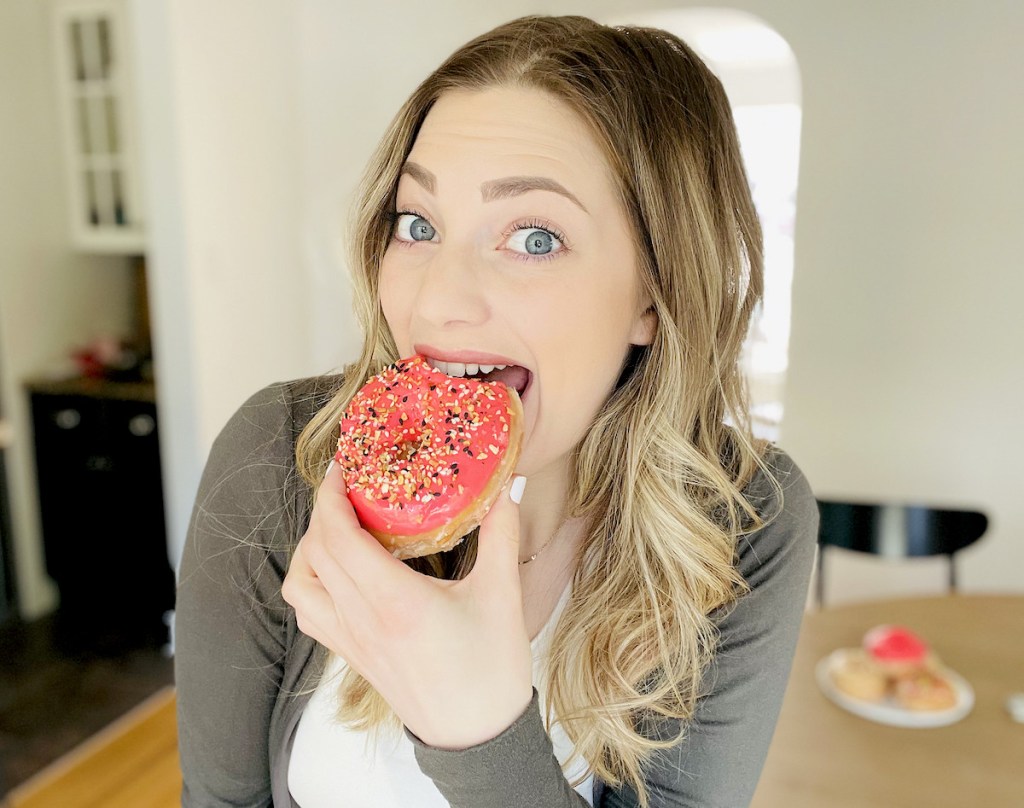 woman biting into pink donut 