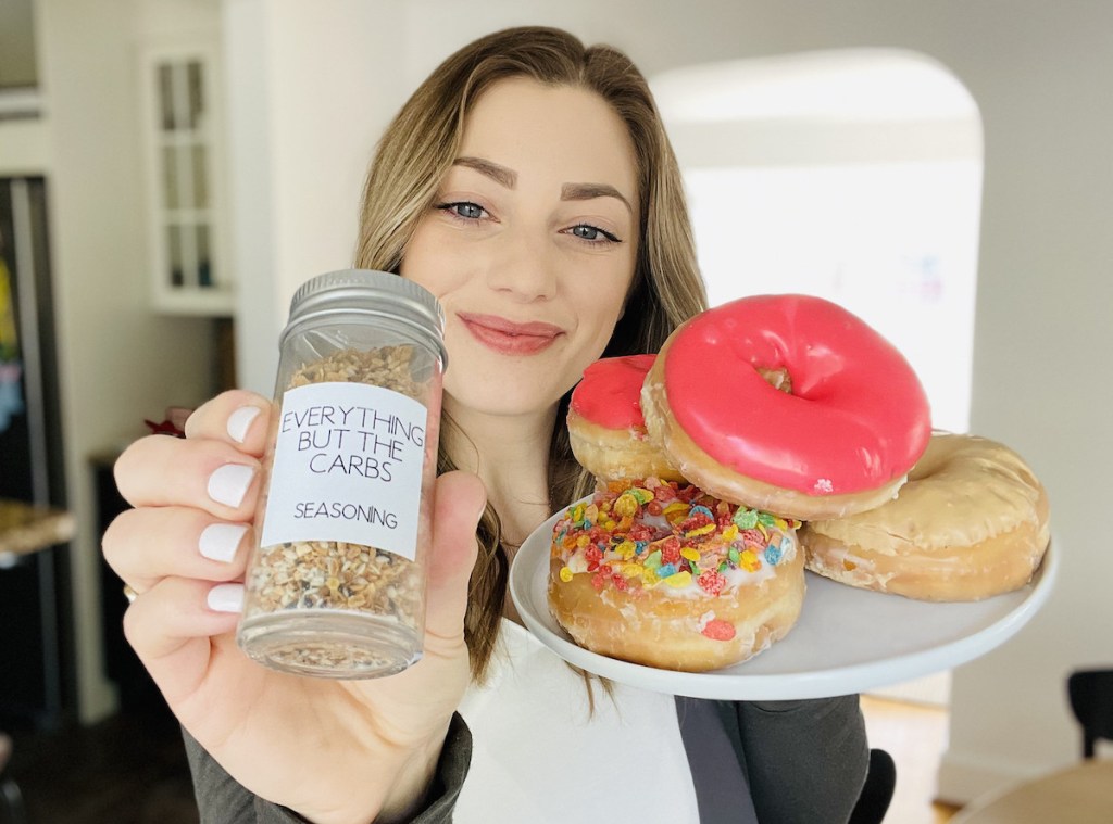 woman holding everything but the carbs seasoning and plate of colorful donuts