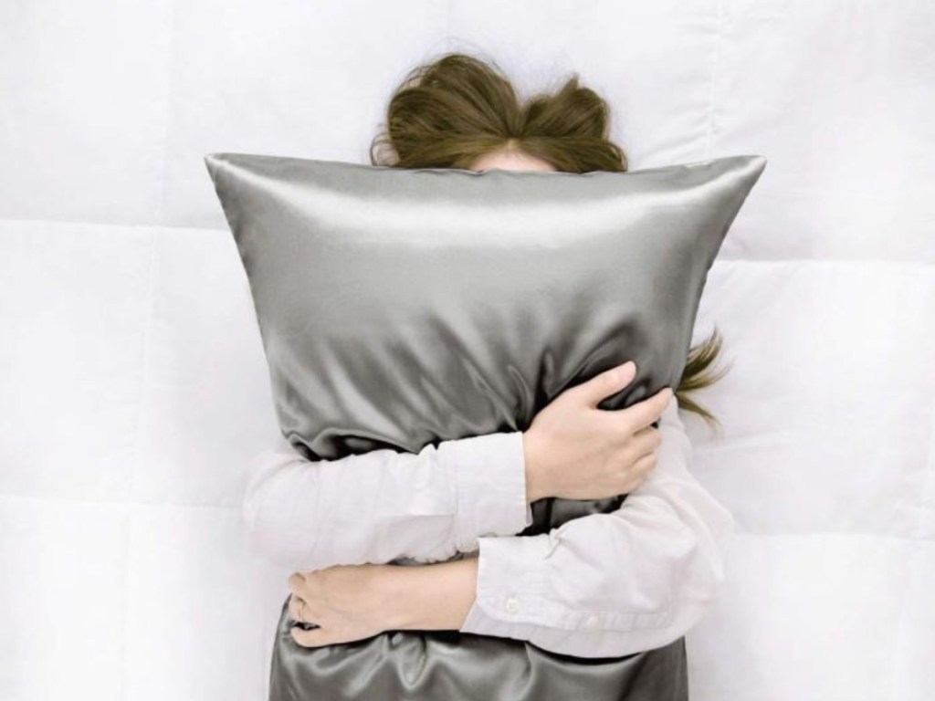 woman covering face with pillow tired and stress