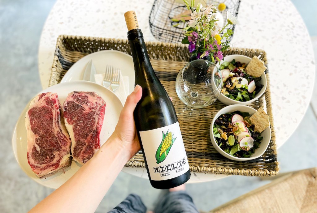 hand holding a bottle of keto wine over tray of steaks and salad