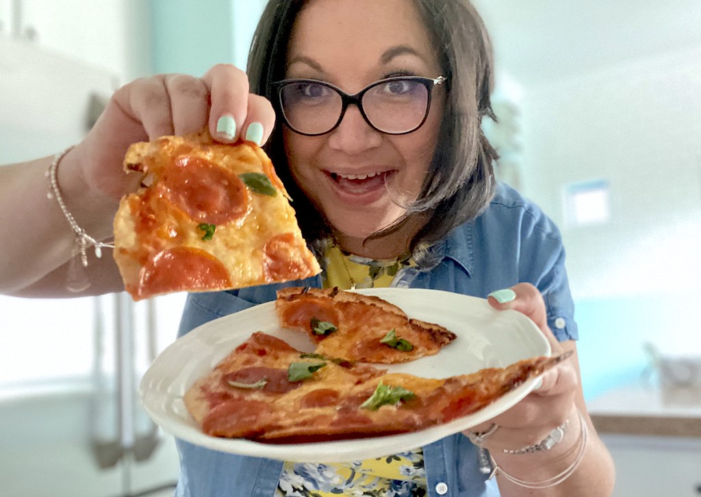 woman holding up slice of keto pepperoni basil pizza