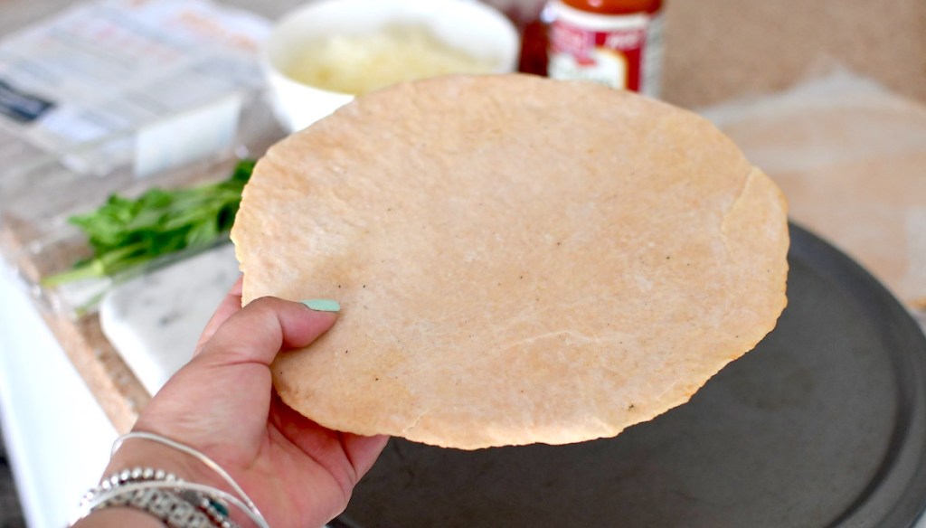 hand holding plain pizza crust over pan