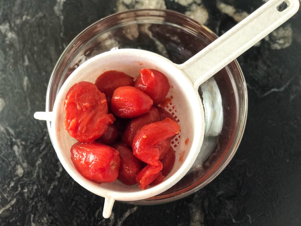 canned whole tomatoes in strainer over a bowl