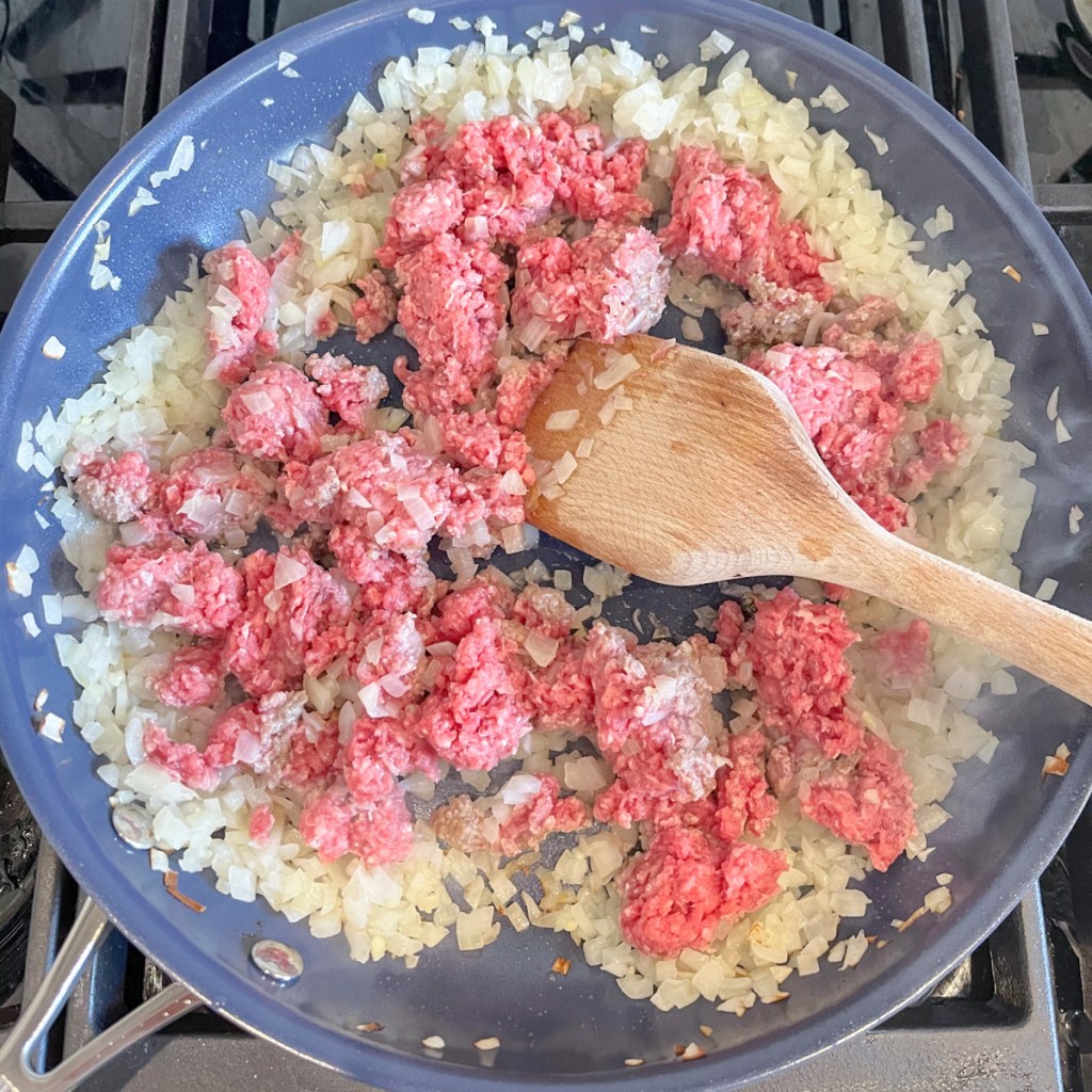 raw ground beef and chopped onion in pan