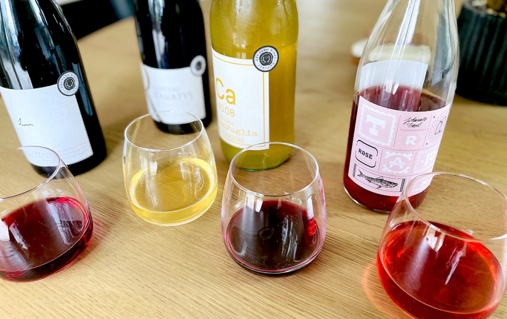 various types of wine bottles and half full glasses sitting on wood table