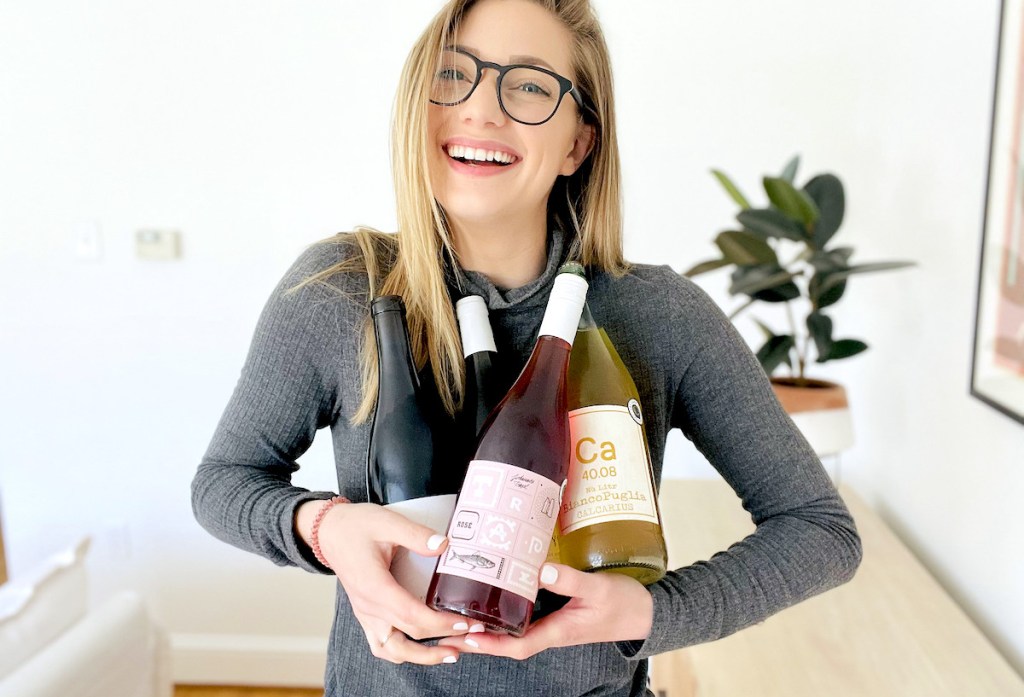 woman laughing holding four bottles of various types of keto wines