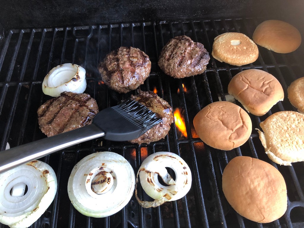 putting burgers on the grill and basting them with butter 