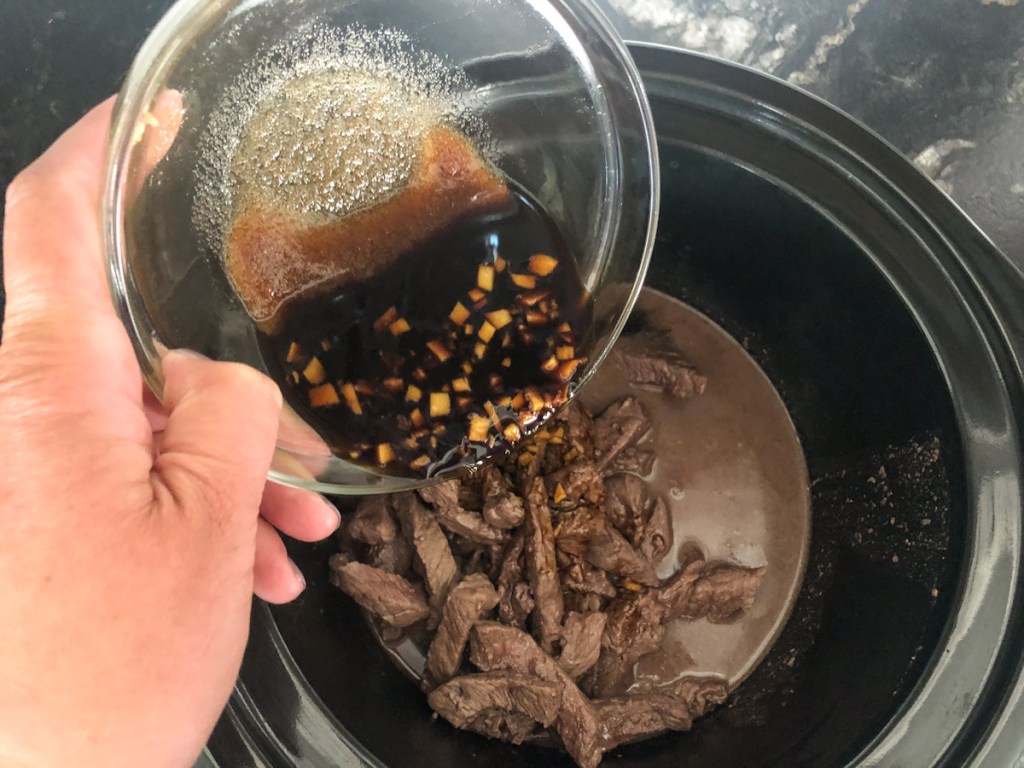 pouring sauce into crockpot over seared steak