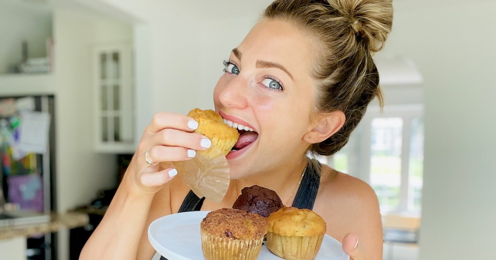 woman holding plate of muffins while biting into keto bakery muffin