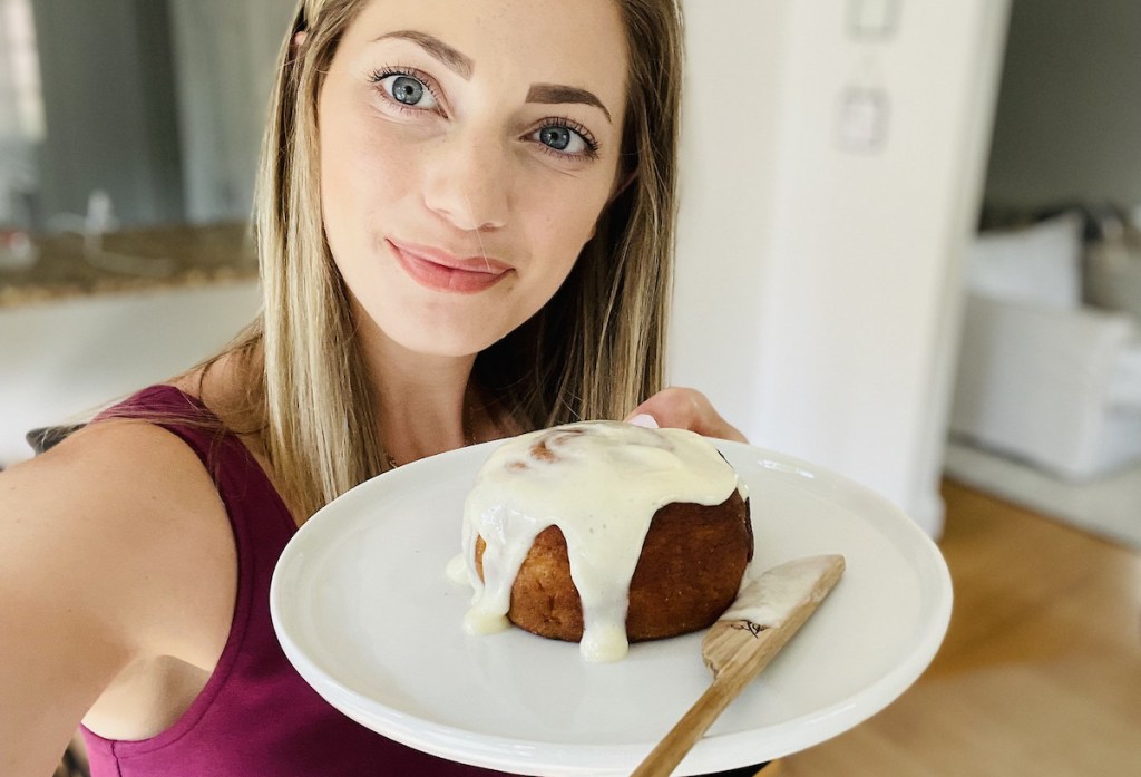 woman holding a plate with wooden knife and keto cinnamon bun with icing