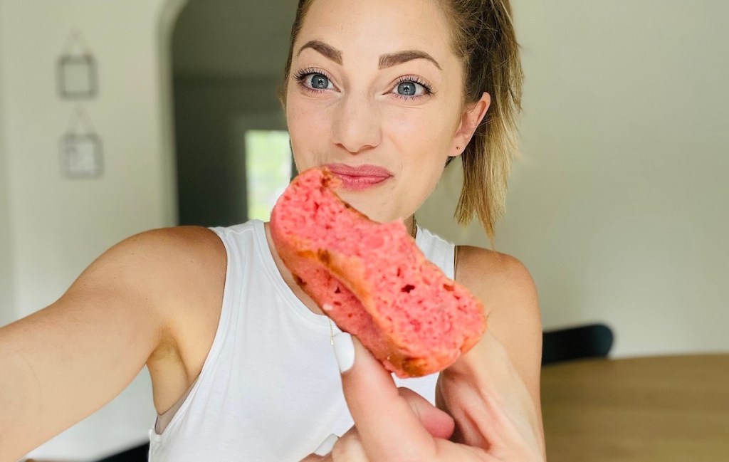 woman holding up half eaten pink donut