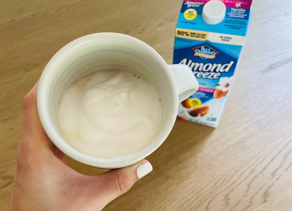 hand holding coffee cup with frothy keto milk inside