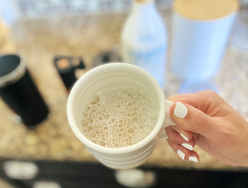 hand holding white coffee mug with bubbles inside