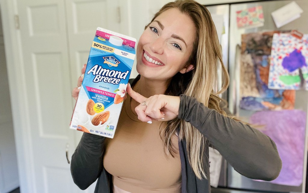 woman holding up carton of almond milk in kitchen