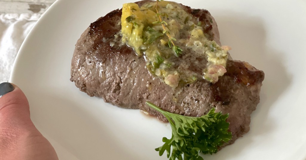 holding plate of steak with cowboy butter on top 