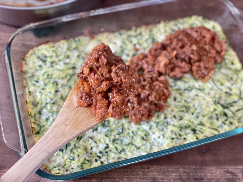 putting meat sauce on crust for keto zucchini pizza casserole