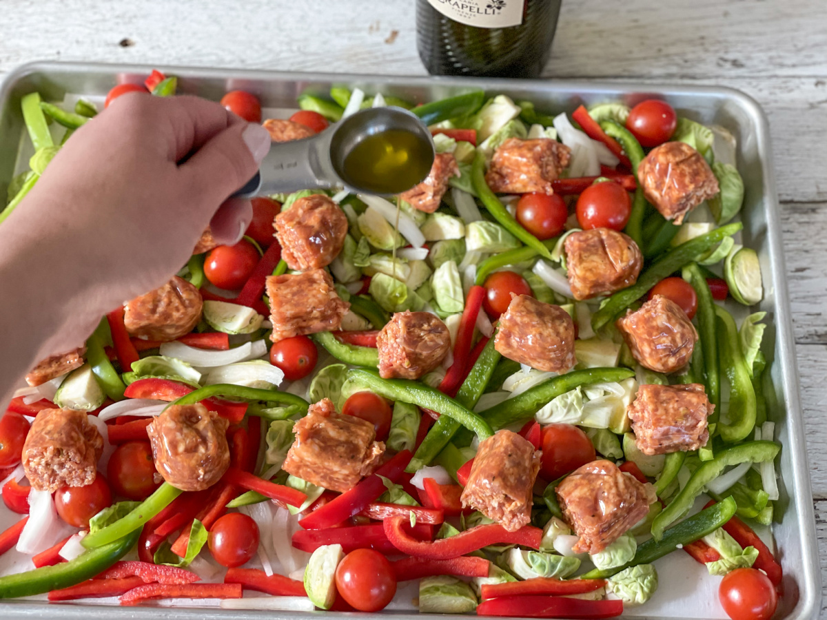 drizzling olive oil on baking sheet with meat and veggies 