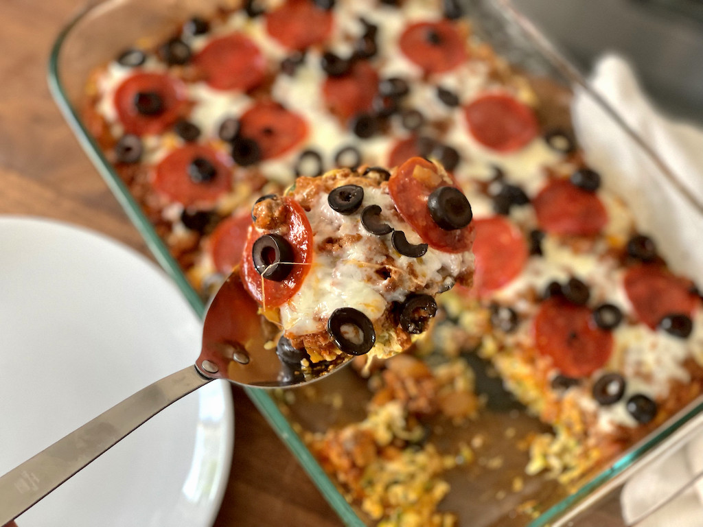 picking up slice of keto pizza casserole with pepperoni and olives 