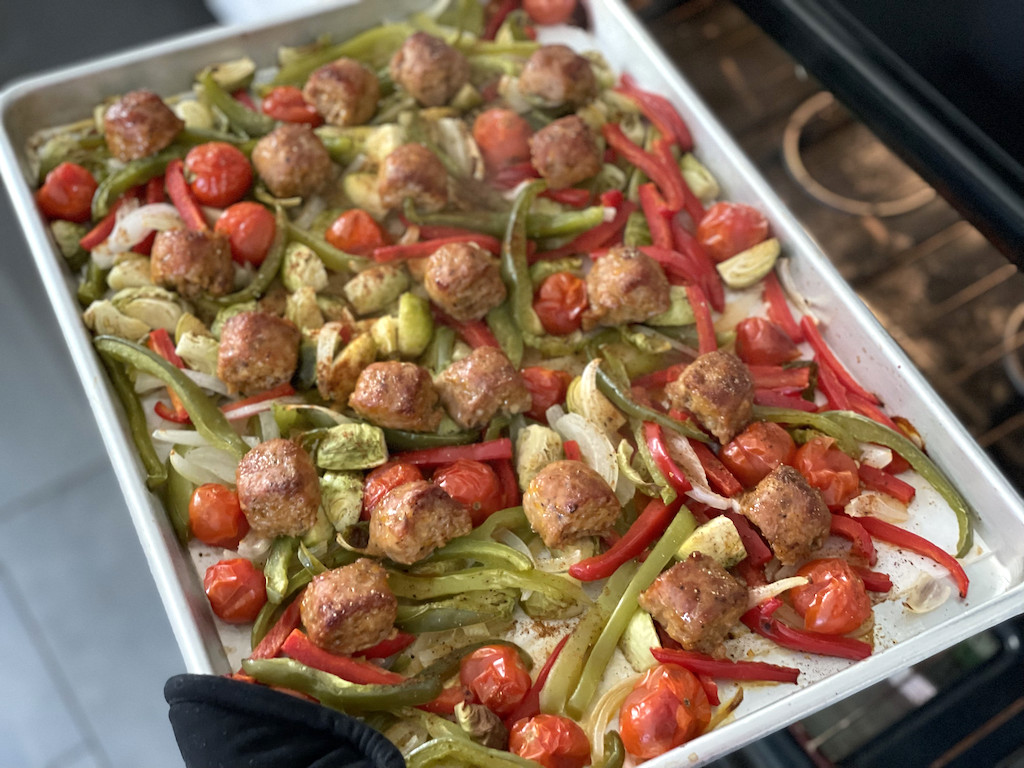 pulling out sheet pan with sausage, peppers, and onions 