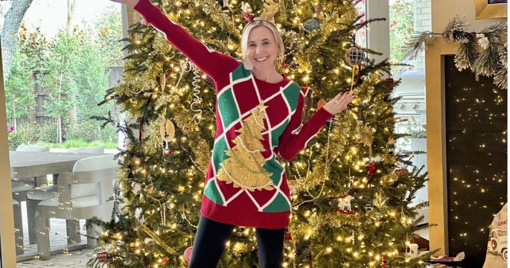 woman wearing a Christmas sweater and standing in front of a Christmas tree