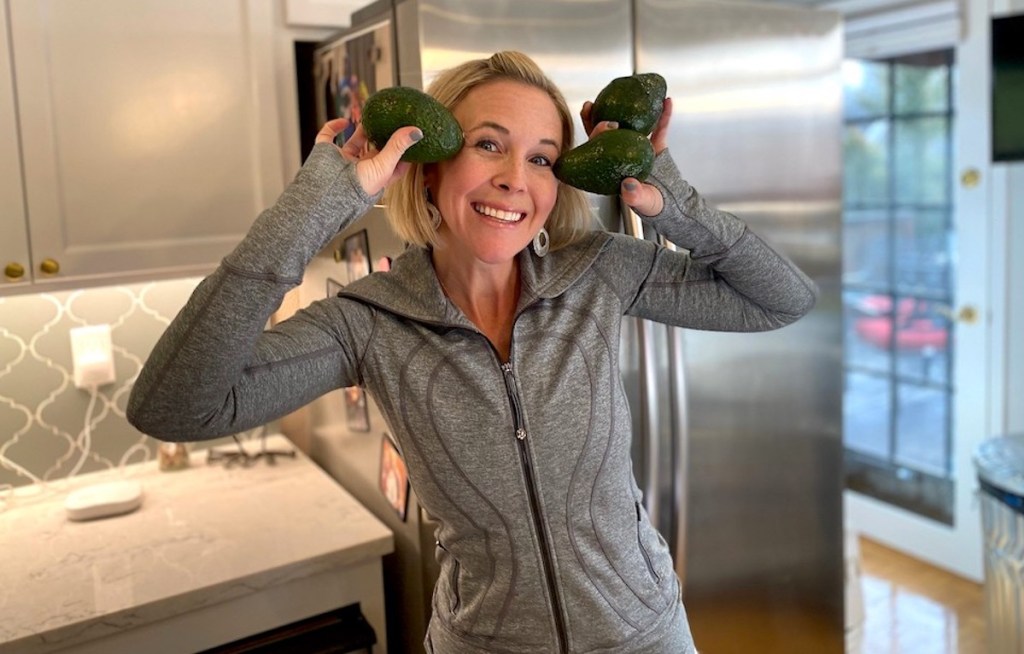woman holding up avocados next to face standing in kitchen