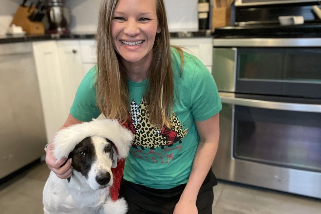 woman wearing a Christmas shirt beside a dog with a Santa hat