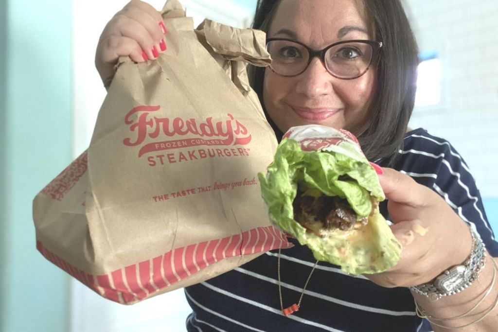 woman holding Freddy's to-go bagand lettuce wrapped sandwich