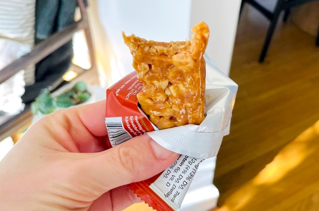 hand holding open wrapper with peanut butter granola bar inside with bite