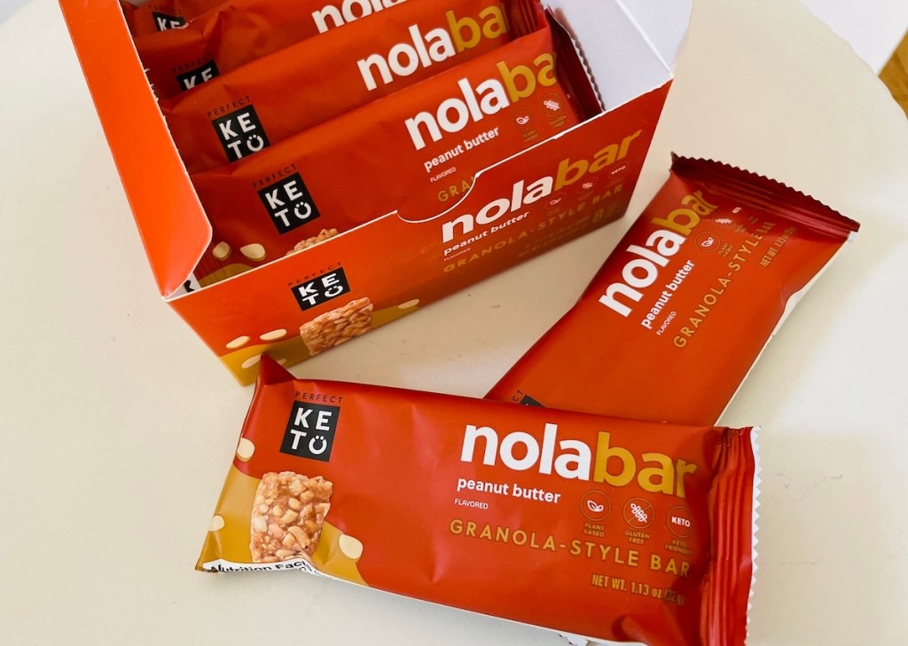 orange nola bars in wrappers and box laying on white table